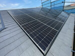 「住宅のスレート屋根に設置された家庭用太陽光パネル。足場と養生ネットを使用した安全施工の様子。」