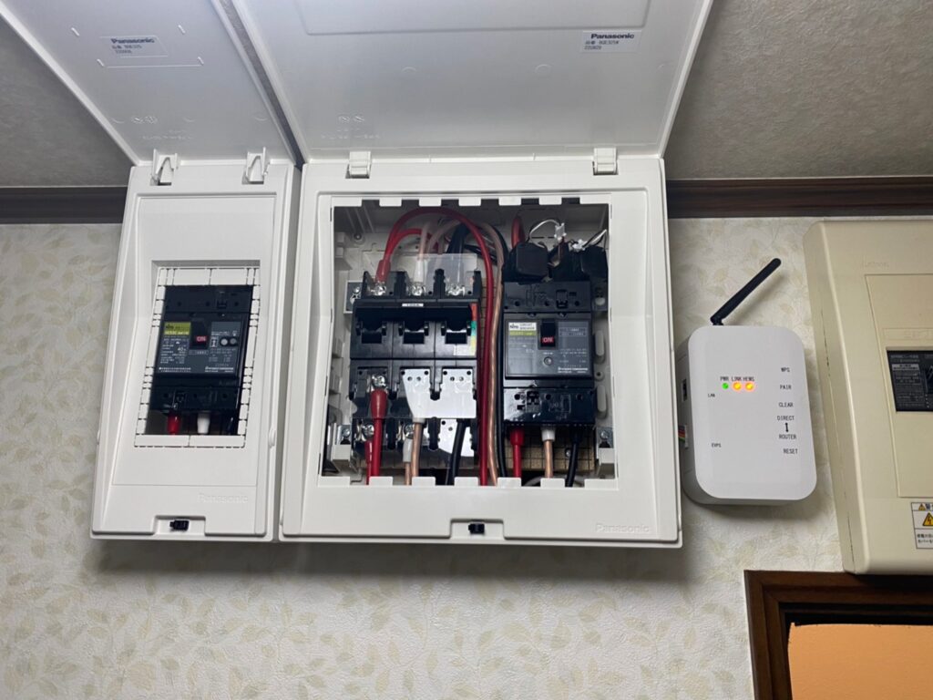 Open electrical distribution panel with multiple circuit breakers and red/black wires; unit labeled Panasonic.