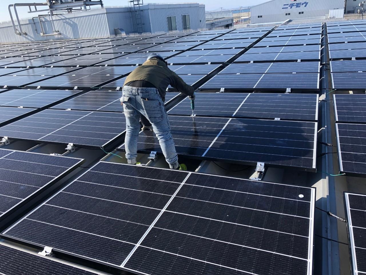 冷凍倉庫屋根上で太陽光パネルを固定している施工状況